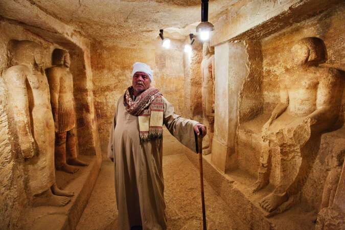 Un gardien prend la pose devant des statues dans une mastaba de la nécropole de Fraser