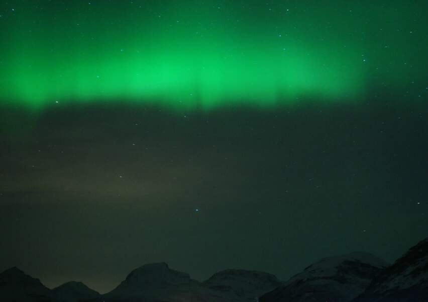Une aurore boréale se dessine au-dessus du relief montagneux de la région de Tromsø, en Norvège du Nord. 