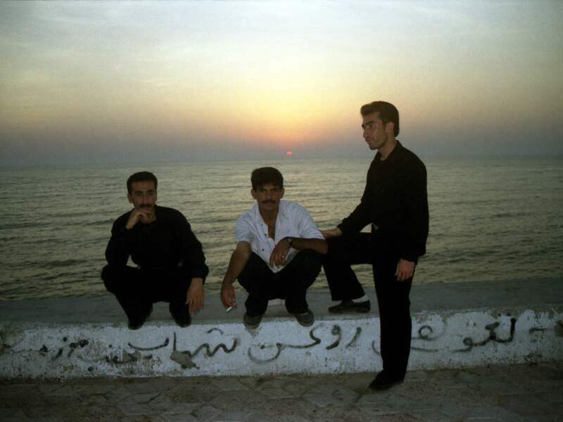 Trois hommes posent près de l'eau au crépuscule, à Bandar-e Anzali, dans la province du Gilan, en Iran