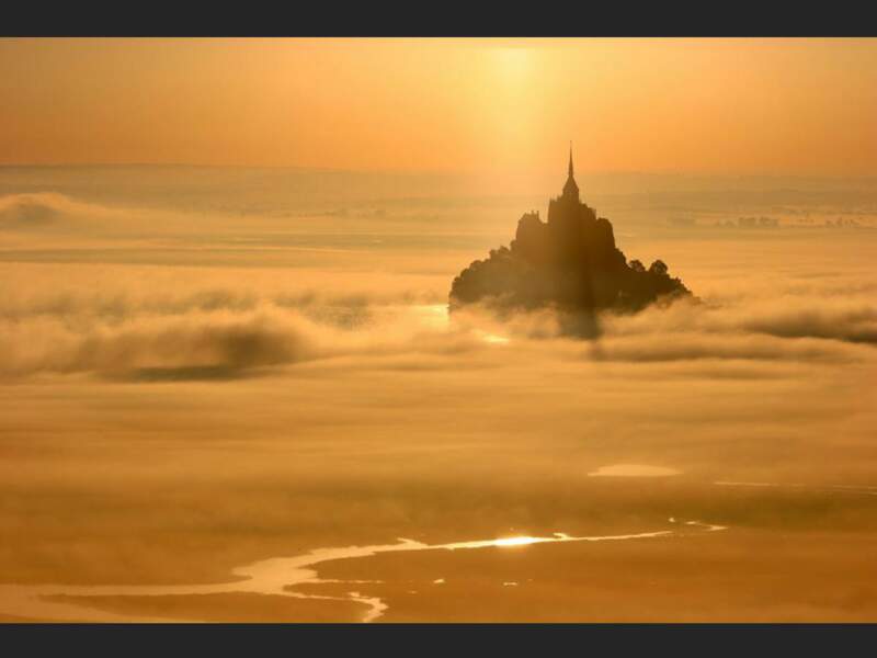 Le Mont-Saint-Michel  se détache dans la brume orangée, en Normandie (France).