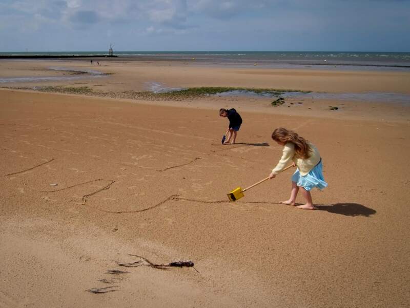 Enfant dessinant des formes sur la plage, à Courseulles-sur-Mer (Calvados, Normandie).
