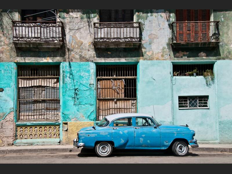Une vieille voiture garée devant une façade colorée et délabrée, une image représentative des rues de La Havane (Cuba).