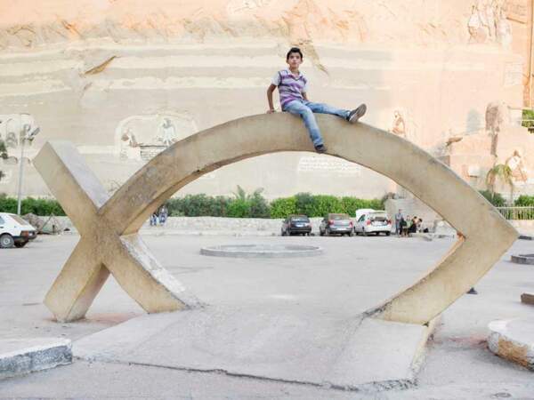 Un enfant de la communauté des « chiffonniers du Caire » se tient sur une sculpture de poisson, en Egypte