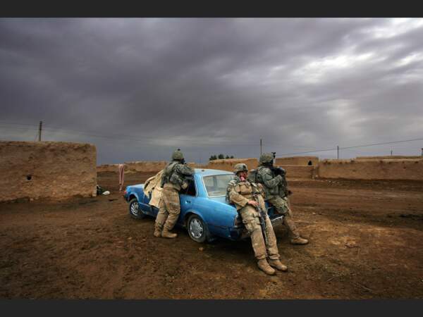 Des soldats américains s’adossent contre une voiture pour se reposer au cours d’une enquête sur des violences entre communautés qui ont provoqué le pillage et l’incendie d’un village. 
