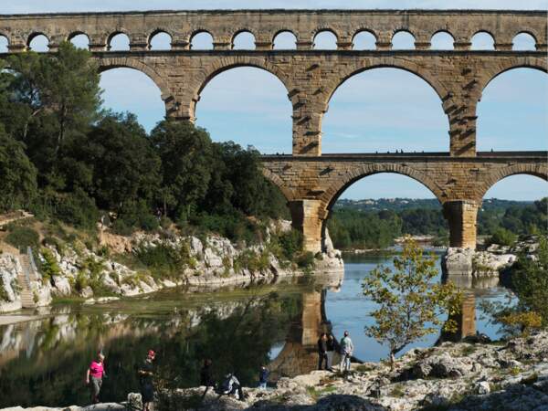 Des visiteurs s’attardent le long du Gardon, la rivière traversée par le Pont du Gard