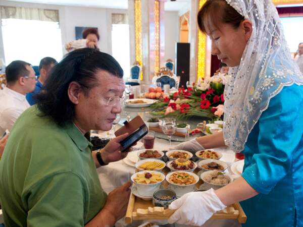 Une serveuse présente un plat à Da Dong lors de l’un de ses voyages