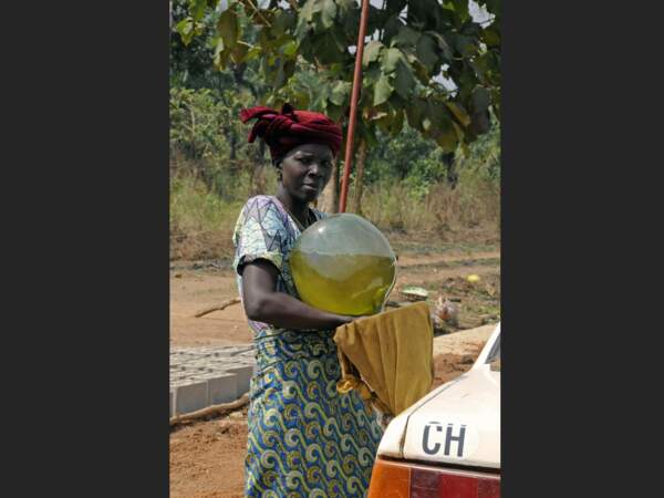 Femme versant de l’essence kpayo dans le réservoir d’une voiture.