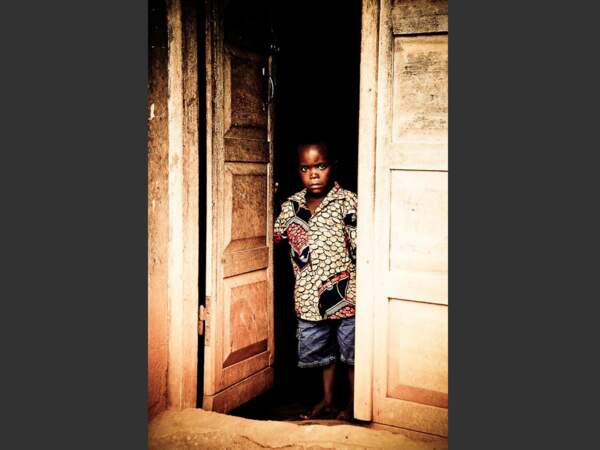 Un jeune garçon se tient dans l'entrebâillement d'une porte, au Togo.