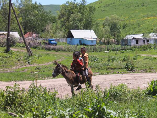 Trois enfants à dos d'âne près d'un village dans le massif du Ferghana, au Kirghizistan
